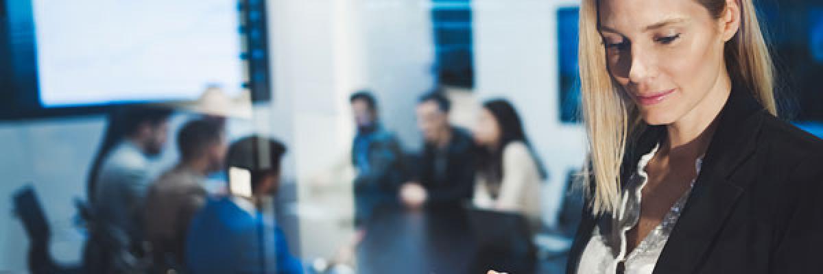 Seguros para Empresas - Mujer joven y rubia de negocios con chaqueta de traje negra y camisa blanca utilizando una tablet en una reunion en la oficina